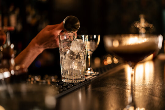 A cocktail being mixed and carefully finished in a bar, presented under warm candlelight.