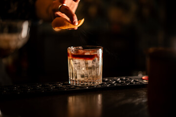 A cocktail being mixed and carefully finished in a bar, presented under warm candlelight.