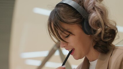 female pens ideas, woman smiles while brainstorming notes, young lady with headphones writes content ideas happily, smiling young woman with headphones jots down creative notes cheerfully