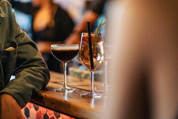 Two freshly served cocktails, including an Espresso Martini, on the bar in a busy cocktail lounge.