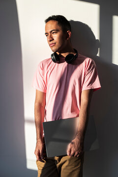 Latino man holding laptop in warm light reflecting thoughtful digital focus