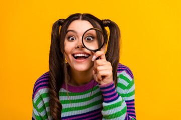 Joyful young woman with magnifying glass in striped sweater against a bold yellow background
