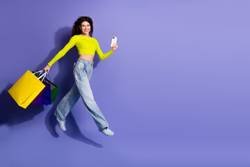 Young woman jumping with shopping bags and taking a selfie neon shirt against a vivid purple...