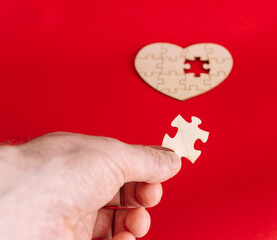 Hand holding puzzle piece matching missing part of wooden heart on red background