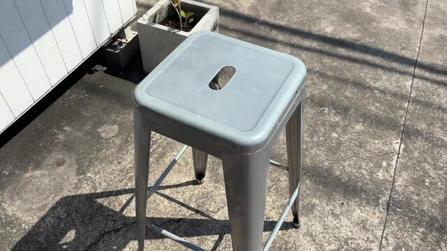 Metal bar stool on cement outdoor sunny day pov shot.