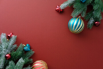 Diagonal corner framing of snow-dusted fir branches and striking red and teal Christmas ornaments