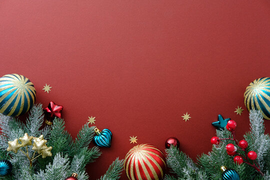 Christmas bottom border of snowy fir branches, red and teal ornaments, and scattered confetti stars. Flat lay, top view.