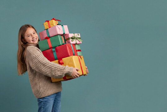 Copyspace, Smiling child carrying a tall stack of colorful wrapped gifts against teal studio background, holiday giving and celebration concept for seasonal advertising and family occasions