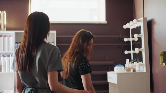 hairdresser helping customer in salon, customer guided to styling chair by experienced salon assistant, professional hairstylist and assistant prepare client for hair styling session in salon