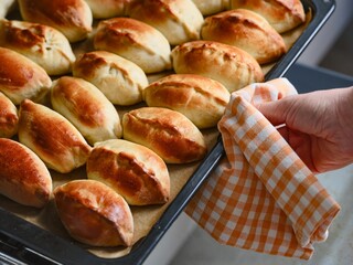 Woman taking baking tray with freshly baked russian pirozhki (pastry) out of the oven