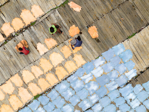 Aerial view of workers amidst a vibrant tapestry of drying materials, where warm peach hues meet cool blues under the sun, Dhaka, Dhaka Division, Bangladesh.