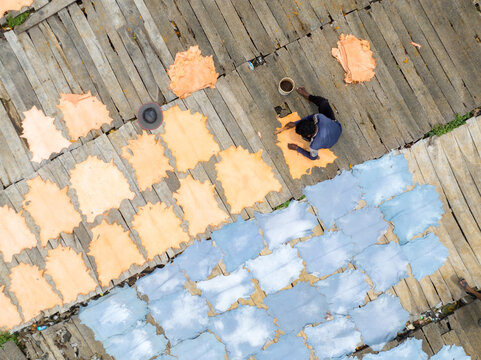 Aerial view of a man treating leather laid out on wooden planks, the hides displaying a spectrum of light tan and blue tones, Dhaka, Dhaka Division, Bangladesh.