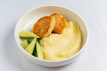 A bowl features creamy mashed potatoes, golden chicken bites, and fresh cucumber slices