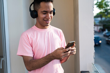 Latino male smiling softly while reading text messages on balcony 