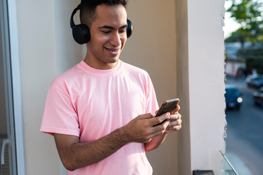 Latino male smiling softly while reading text messages on balcony 