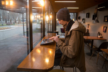  remote workers. Working from Anywhere.  a young man is working on a laptop in a cafe and drinking coffee