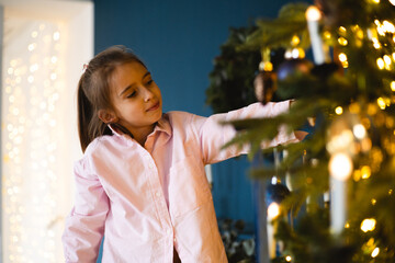 Young girl decorates Christmas tree at home with joy during festive season in early December