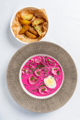 A vibrant beet soup topped with slices of egg and herbs, accompanied by golden potato wedges