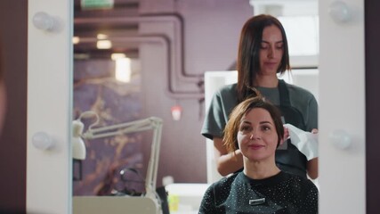 white stylist with white client applying color in salon mirror, hands in gloves working on hair while client smiles in cape, gentle consultation and careful technique, foils and products on counter,