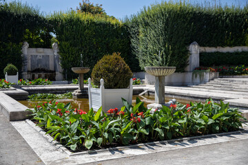 Classical garden with fountains, green hedges, and blooming flower beds. Neatly arranged space with water and symmetrical design on a sunny day.