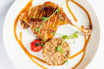 A succulent roasted chicken leg, accompanied by a flavorful rice dish and a bright cherry tomato