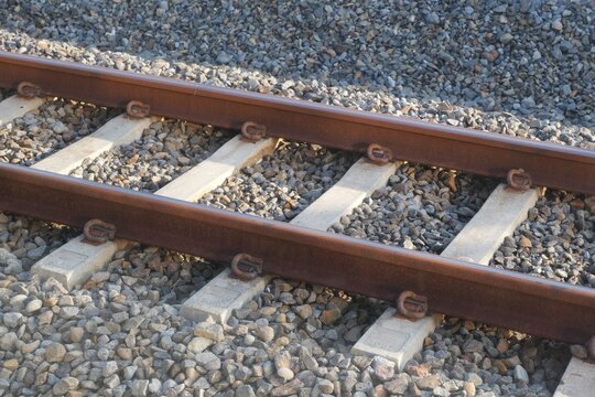 Detailed view of rusty railway tracks supported by concrete sleepers and surrounded by gravel ballast, used in train transportation systems.
