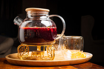 Herbal tea steams in a glass pot beside chic cups on a wooden tray, creating coziness