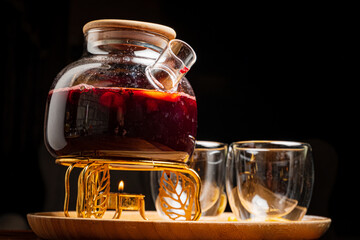 A rich, steaming drink brews in a glass pot, glowing warmly on a wooden tray at dusk