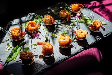 Savory shrimp appetizers arranged beautifully on a dark platter, decorated with greens and flowers