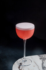 A vibrant cocktail with a frothy top rests elegantly on a marble surface, exuding freshness