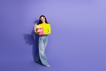 Young woman in neon top holds popcorn bucket and smiles against purple background for a fun casual fashion lifestyle shoot