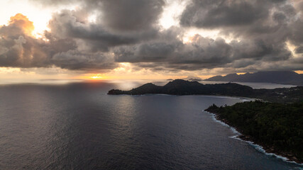 Sunset over the calm ocean and hilly coastline, framed by clouds, creating a tranquil scene. Seychelles, Mahe.