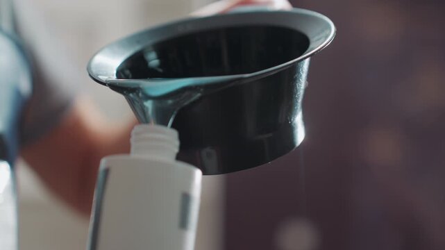 closeup of bottle and funnel during treatment, preparation of liquid treatment with precise pouring into funnel, careful handling of solution during salon refilling process with closeup focus