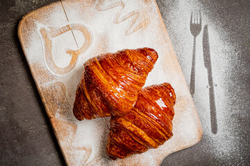 Freshly baked croissants with a golden crust, elegantly displayed on a wooden board with flour dust