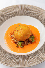 A delicious fritter sits elegantly on a vibrant tomato sauce, garnished with herbs for flavor