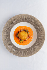 A stunning dish features a golden croquette atop vibrant sauce and fresh herbs