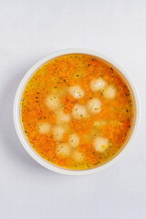 A steaming bowl of vibrant orange soup filled with fluffy dumplings and sprinkled with fresh herbs