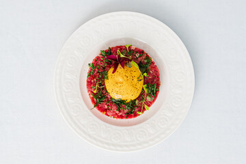 Beef tartare topped with a rich egg yolk sits elegantly on a white plate, showcasing artistry