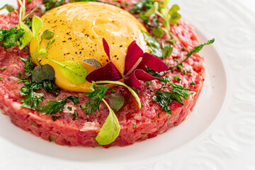 A dish of finely chopped beef topped with a bright yolk and fresh herbs