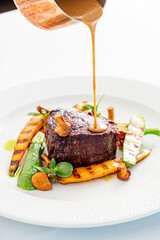 A chef drizzles rich sauce over a juicy steak, garnished with vibrant grilled veggies