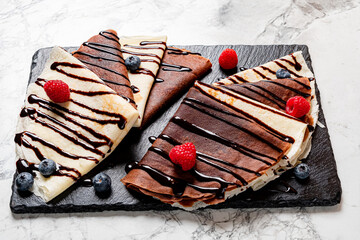 Tempting crepes with chocolate drizzle and fresh raspberries displayed elegantly on a black slate