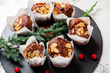 Six chocolate muffins with almond slices on a dark platter, topped with festive greenery