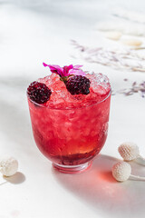 A vibrant cocktail with ice and berries, adorned with a flower on a cheerful table