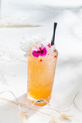 A beautifully crafted cocktail with vibrant flowers and ice sits elegantly on a sunny table