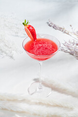 A vibrant red cocktail with a fresh strawberry sits elegantly on a light surface