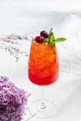 Bright red cocktail garnished with mint and berries, set against pastel florals, perfect for summer