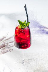A refreshing red drink, garnished with mint leaves, sits elegantly in a glass with ice