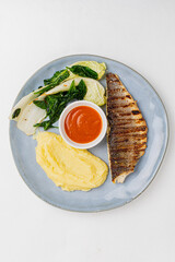 A vibrant plate featuring grilled fish, smooth mashed potatoes, fresh greens, and tangy sauce