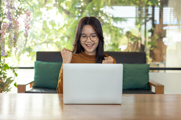 Naklejka premium Smiling woman celebrating success while using a laptop in a bright cozy space, expressing achievement, positivity, motivation, and a productive modern lifestyle.