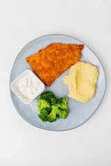 A delicious plate features crispy fried fish, smooth mashed potatoes, fresh broccoli, and sauce